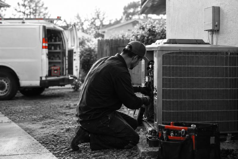 HVAC technician servicing an outdoor air-conditioning unit beside a work van