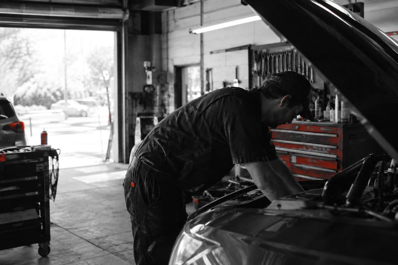 Mechanic working under the hood of a car in a small independent garage
