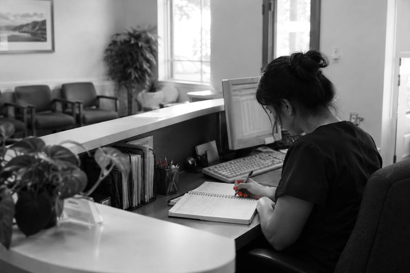 Receptionist writing in a paper appointment book at a small clinic front desk